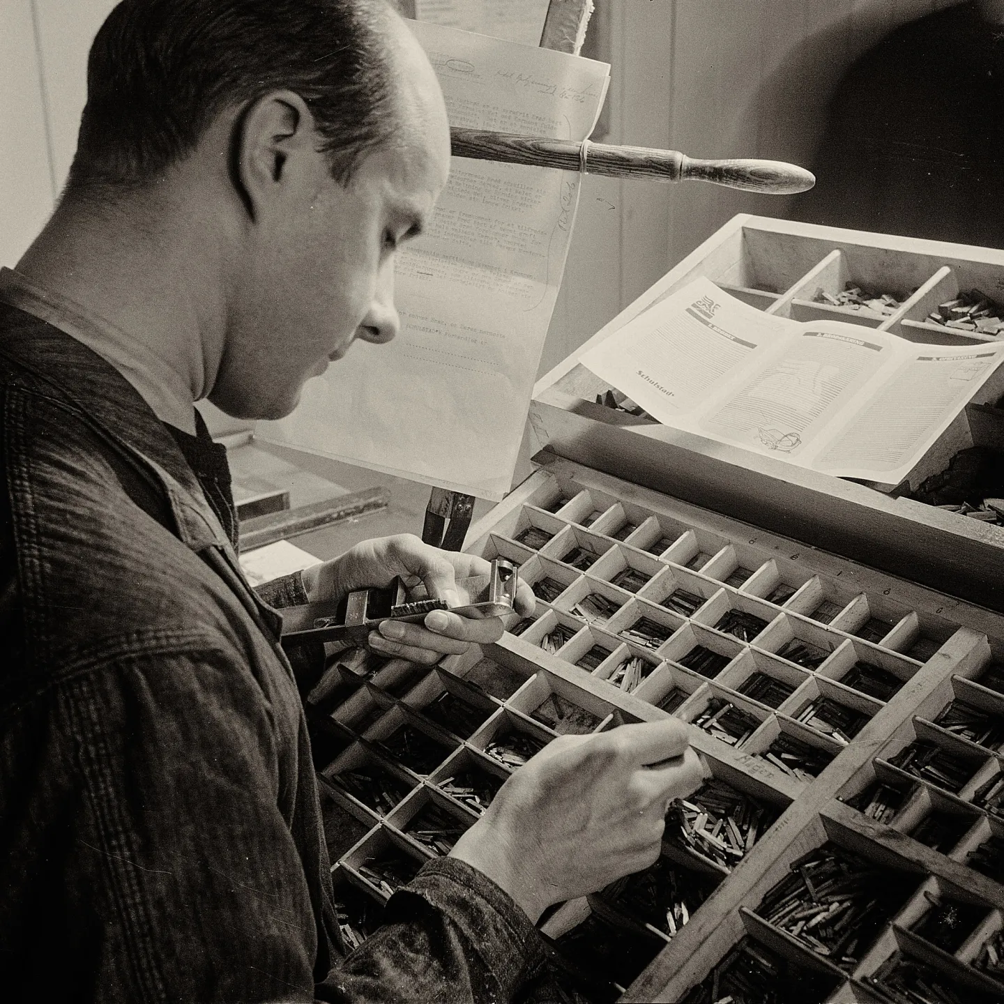 Black-and-white photo of a typesetter hand-setting metal type from a wooden type case.